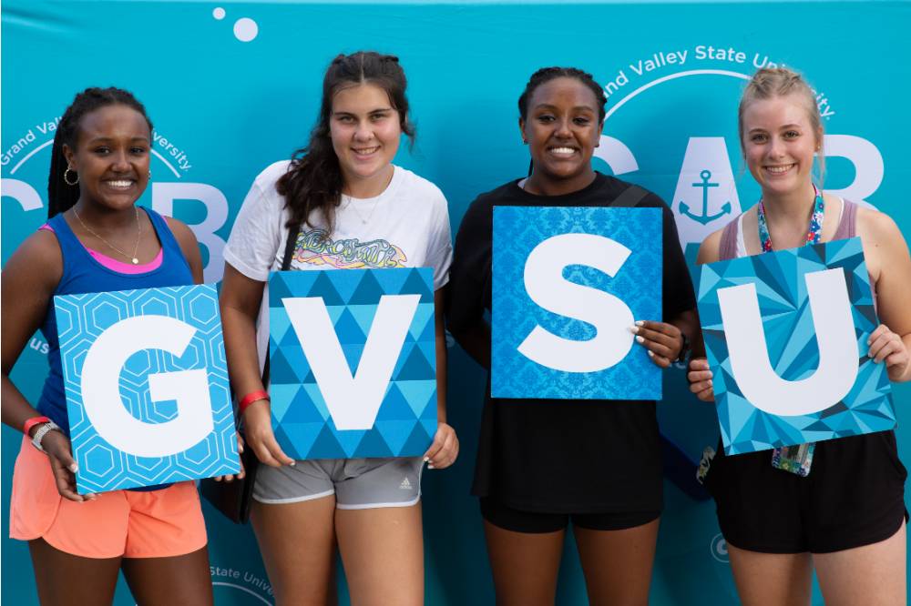 four students posing in front of CAB backdrop at Laker Kickoff photo booth holding GVSU letters